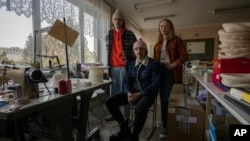 Co-founders of Ukrainian high-end hat designer brand Ruslan Baginskiy 'RB', from left, Petro Yasinskiy, Ruslan Baginskiy and Victoria Semerei, pose for a photo inside a classroom they turned into a workshop, in Lviv, western Ukraine, March 25, 2022. 