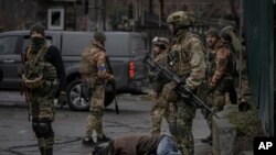 Binh sĩ Ukraine kiểm tra thi thể của những thường dân ở vùng ngoại ô Kyiv do quân Nga chiếm đóng trước đó xem có bị gài mìn không, ngày 2 tháng 4 năm 2022.
