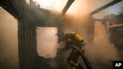 A Ukrainian firefighter sprays water inside a house destroyed by shelling in Kyiv, Ukraine, March 23, 2022.