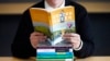 FILE - Amanda Darrow, director of youth, family and education programs at the Utah Pride Center, poses with books that have been the subject of complaints from parents in recent months, in Salt Lake City, Dec. 16, 2021. 