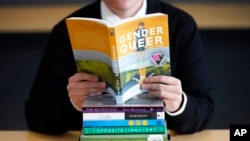 FILE - Amanda Darrow, director of youth, family and education programs at the Utah Pride Center, poses with books that have been the subject of complaints from parents in recent months, in Salt Lake City, Dec. 16, 2021. 