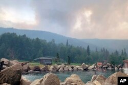 Asap dari Kebakaran hutan Munson Creek membubung di belakang Chena Hot Springs Resort saat para tamu menonton dari kolam batu terbuka di dekat Fairbanks, Alaska, pada Senin, 5 Juli 2021. (Divisi Kehutanan Alaska via AP)