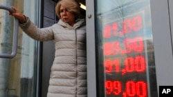 FILE - In this Feb. 24, 2022, photo, a woman leaves an exchange office with a screen showing the currency exchange rates of US dollar and Euro to Russian rubles in Moscow.