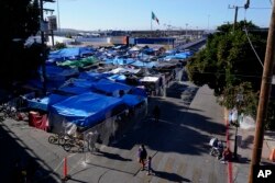 FILE - Migrants walk outside a camp that blocks the entrance to a pedestrian crossing into the United States, Nov. 8, 2021, in Tijuana, Mexico.