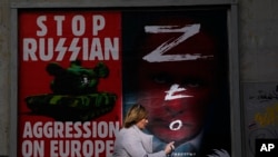 A woman walks past a wall with posters depicting Russian President Vladimir Putin, right, in Warsaw, Poland, March 24, 2022. 
