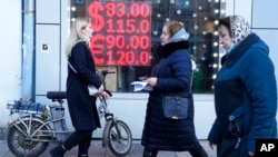 FILE - People walk past a currency exchange office screen displaying the exchange rates of the US dollar and euro to Russian rubles in Moscow, on Feb. 28, 2022. 