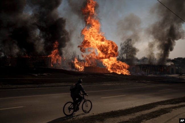 A man rides his bike past flames and smoke rising from a fire following a Russian attack in Kharkiv, Ukraine. (AP Photo/Felipe Dana)