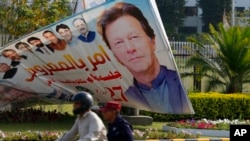 Seorang pengendara sepeda motor melewati papan reklame dengan gambar Perdana Menteri Pakistan Imran Khan yang dipajang di luar Majelis Nasional, di Islamabad, Pakistan, 3 April 2022. (Foto: AP)