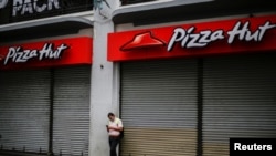 Un hombre revisa su teléfono junto a un local de la franquicia Pizza Huts en San José, capital de Costa Rica, cerrado por la pandemia de COVID-19 en julio de 2020.