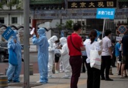 Medical staff in protective gear carry signs to assist people who live near or who have visited the Xinfadi Market, a wholesale food market where a new COVID-19 coronavirus cluster has emerged, as they arrive for testing in Beijing, June 17, 2020.