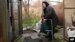Olga Lehan, 71, walks outside her house in Demydiv, Ukraine, Nov. 2, 2022. Her home near the Irpin River was flooded when Ukraine destroyed a dam to prevent Russian forces from storming Kyiv early in the war. Weeks later, the water from her tap turned brown from pollution.