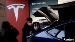 FILE - Visitors wearing face masks check a China-made Tesla Model Y sport utility vehicle (SUV) at the electric vehicle maker's showroom in Beijing, China, Jan. 5, 2021.