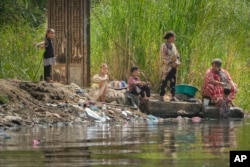 Seorang wanita dan anak-anaknya membersihkan piring di samping sampah plastik di tepi Sungai Nil di Kairo, Mesir, Kamis, 29 September 2022. (AP Photo/Amr Nabil)