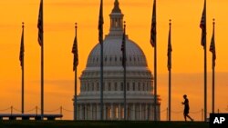 Siluet pejalan kaki dberjalan melewati bendera AS di National Mall dan melewati US Capitol Building di Washington, 7 November 2022. (Foto: AP)