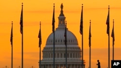 La silueta de un peatón temprano en la mañana contra el amanecer mientras camina frente a las banderas de EEUU en el National Mall y pasa por el edificio del Capitolio en Washington, el 7 de noviembre de 2022.