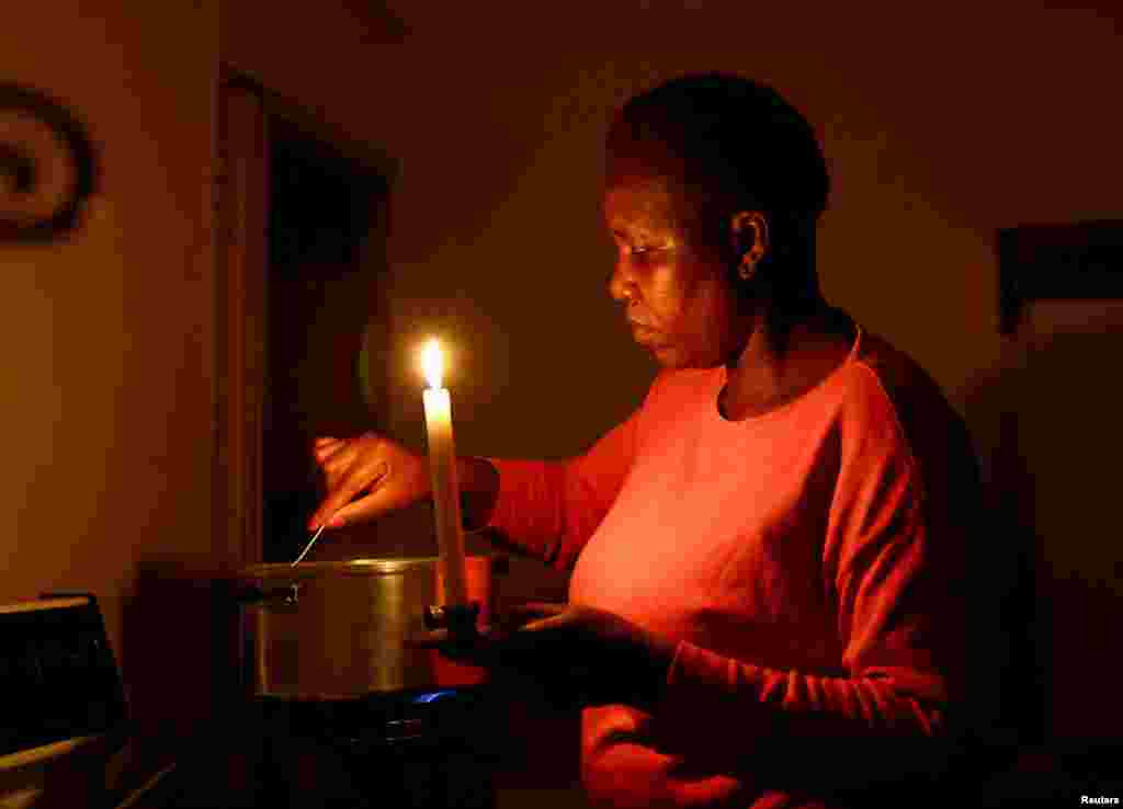 Maria Modiba cooks by a candlelight during one of the frequent power outages from South African utility Eskom, caused by its aging coal-fired plants, in Soweto, South Africa November 11, 2022.