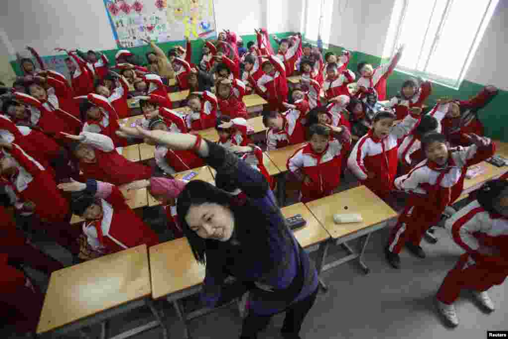 Seorang guru terpaksa mengajar muridnya melakukan olahraga senam kesegaran jasmai di kelas akibat polusi yang menutupi udara di Jinan, provinsi Shandong (14/1). 