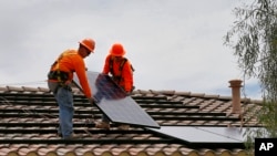 FILE - Electricians install solar panels on a roof for Arizona Public Service company in Goodyear, Arizona, July 28, 2015.