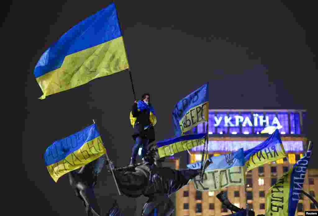 A pro-European integration protester waves a Ukrainian national flag as she stands on a statue during a rally in Independence Square in Kiev, Dec. 15, 2013. 