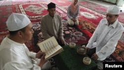 A Muslim man from the Chinese Hui minority reads the Koran as others listen in a sitting room in Aksu, Xinjiang Uighur Autonomous Region, July 27, 2012.