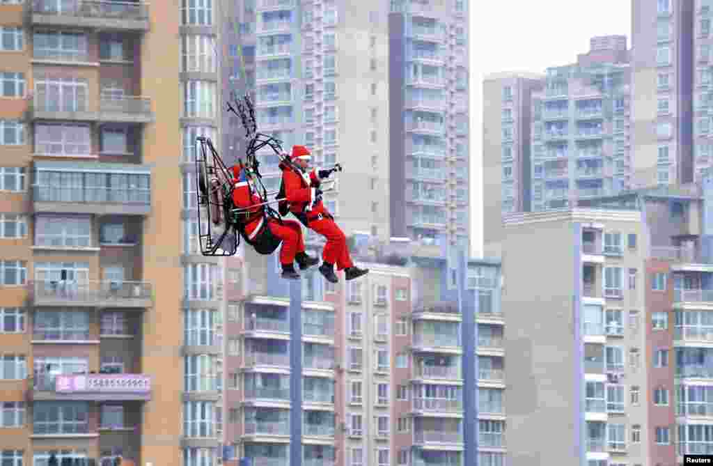 Members of a local powered parachute club wearing Santa Claus costumes fly past residential buildings to drop presents to pedestrians during a promotional event celebrating Christmas in Guiyang, Guizhou province, China, Dec. 24, 2014.