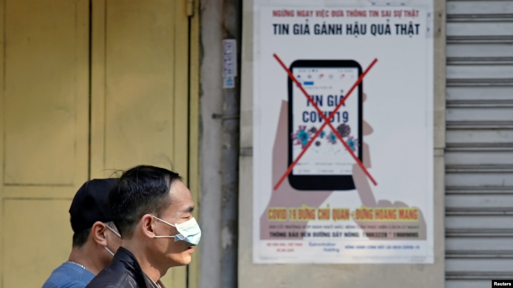 Người dân đeo khẩu trang đi qua một áp phích cảnh cáo về việc phát tán "tin giả" trên mạng về virus corona ở Hà Nội hôm 14/4. Một nghị định mới vừa được đưa ra để xử phạt những người vi phạm điều này.