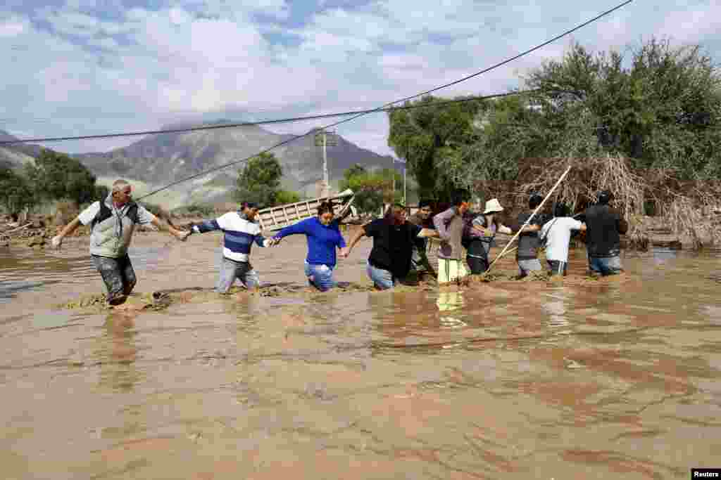 Locals cross a flooded river in Copiapo city, Chile. The number of deaths rose to four after rains battered the north and caused flooding, the government said, while 22 others were unaccounted for as the military rescued stranded villagers.