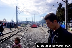 A man walks amid a makeshift encampment, with tents set up between train tracks in the northern Greek border town of Idomeni, March 4, 2016. (J. Dettmer for VOA)