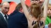 A topless demonstrator with written messages on her back walks towards Russian President Vladimir Putin (L) and German Chancellor Angela Merkel (R) during the opening tour in Hannover, Germany, April 8, 2013. 