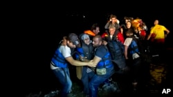 Two Syrian refugees try to carry an elderly woman off a dinghy as it arrives from the Turkish coast to the northeastern Greek island of Lesbos, Oct. 6 , 2015. 