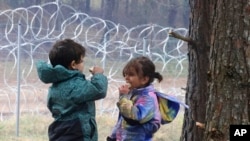 Migrant children eat near the barbed wire fence as migrants gather at the Belarus-Poland border near Grodno, Belarus, Nov. 13, 2021