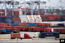 FILE - Two trucks move shipping containers at the Port of Long Beach, Feb. 17, 2015, in Long Beach, California.