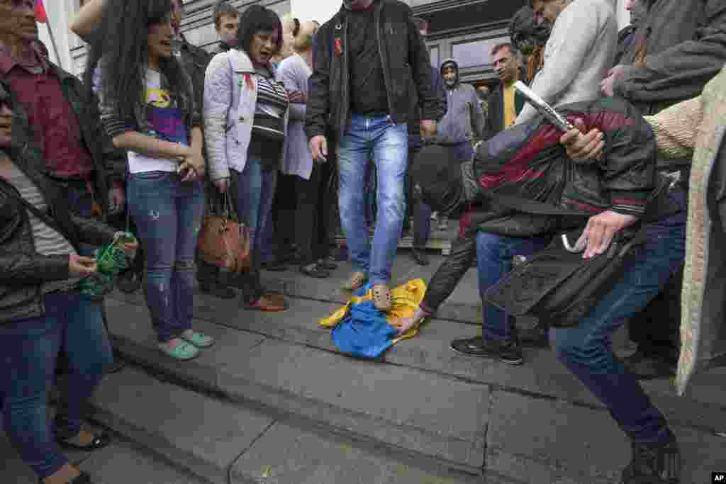 Pro-Russian activists trample a Ukraine flag as other celebrate the capture of an administration building in the center of Luhansk, Ukraine, one of the largest cities in Ukraine's troubled east, Tuesday, April 29, 2014.