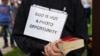 A priest holds a bible and a sign reading &quot;God Is Not A Photo Opportunity&quot; as President Donald Trump&#39;s motorcade passes on the way to the nearby Saint John Paul II National Shrine in Washington, D.C., while protests continue against the death of George Floyd in Minneapolis police custody.