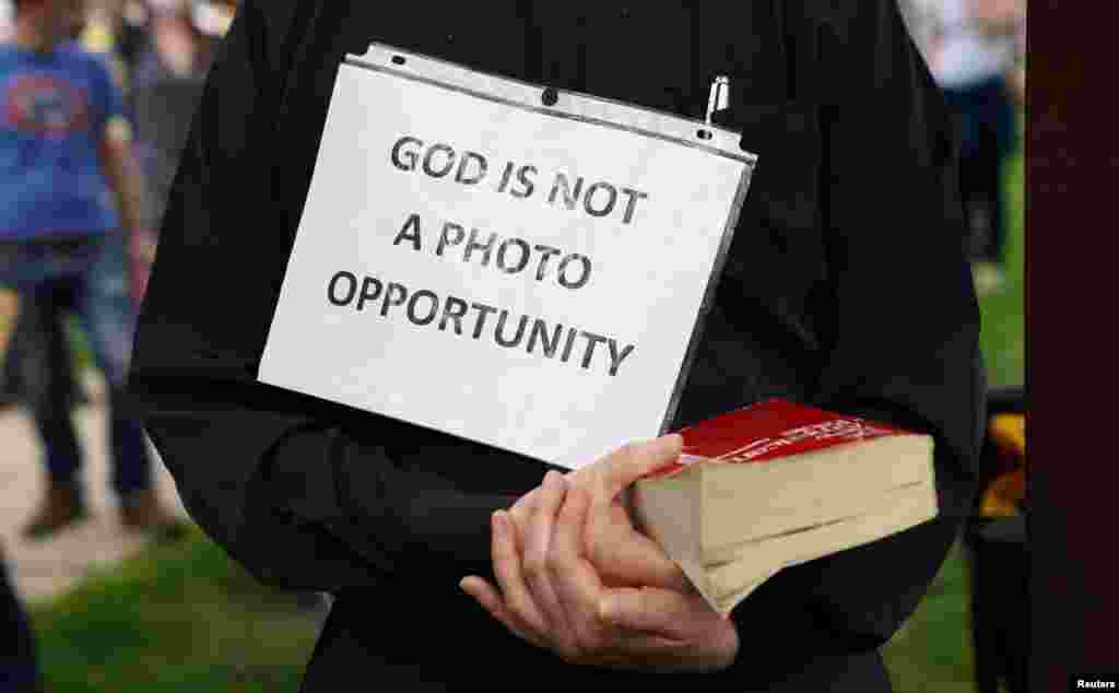 A priest holds a bible and a sign reading &quot;God Is Not A Photo Opportunity&quot; as President Donald Trump&#39;s motorcade passes on the way to the nearby Saint John Paul II National Shrine in Washington, D.C., while protests continue over the death of George Floyd, who died while being held by in Minneapolis police.