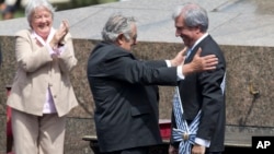 Uruguay's outgoing President Jose Mujica, center, reaches out to new President Tabare Vazquez during Vazquez's inauguration ceremony at Independence Plaza in Montevideo, March 1, 2015. 