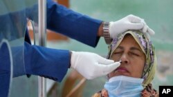 ঢাকায় একটি পরীক্ষা কেন্দ্রে একজন স্বাস্থ্যকর্মী কোভিড-১৯ পরীক্ষা করার জন্য এক নারীর কাছ থেকে নমুনা সংগ্রহ করছেন। ৩০ জানুয়ারি ২০২২।