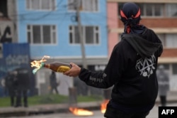Un manifestante arroja un cóctel Molotov a la policía antidisturbios durante una protesta contra el gobierno del presidente colombiano Iván Duque para conmemorar el primer aniversario de un estallido social, frente a la Universidad Nacional en Bogotá, el 28 de abril de 2022.