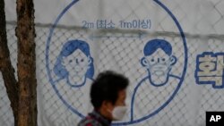 A woman wearing a face mask to help curb the spread of the coronavirus passes by a sign reminding the precautions to take against the coronavirus at a park in Seoul, South Korea, April 29, 2022.