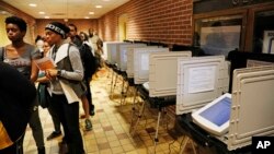 Voters wait in line on election day next to unused machines as the precinct switched over to paper ballots after a judge ordered the polling location to remain open until 10 p.m., in Atlanta, Nov. 6, 2018. 