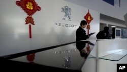 Seorang staf penjualan tengah menunggu pelanggan di ruang pamer bersama mobil-mobil China Dongfeng dan Peugeot di Beijing, Rabu (19/2).