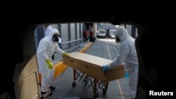 Trabajadores de una funeraria transportan el cuerpo de una persona que murió a causa del coronavirus dentro de un sarcófago de cartón, en la ciudad de México. Junio 5 de 2020.