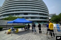 Warga antre untuk tes COVID-19 di lokasi pengujian di kompleks perkantoran di Beijing, Jumat, 29 April 2022. (Foto: AP)