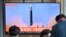 People watch a television screen showing a news broadcast with file footage of a North Korean missile test, at a railway station in Seoul on May 4, 2022. - North Korea fired a ballistic missile on May 4, South Korea's military said, just a week after lead