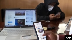 FILE: A person browses social media platforms on his mobile phone with a member of his outfit of social media influencers at an office in Thika town, central Kenya on April 26, 2022. 