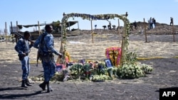 FILE: Ethiopian federal police officers guarding the site look at a flower memorial bearing portraits of victims at the crash site of an Ethiopian airways operated Boeing 737 MAX aircraft on March 16, 2019 in Ethiopia.