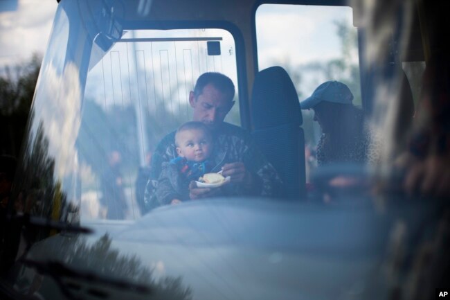 A man feeds a child as they arrive by bus at a reception center for displaced people in Zaporizhzhia, Ukraine, Monday, May 2, 2022. (AP Photo/Francisco Seco)