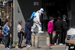 A worker in a protective suit sprays disinfectant as residents wearing face masks line up for mass coronavirus testing outside a residential complex, in Beijing, May 3, 2022.