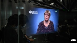 A journalist wearing a face mask as a preventive measure against COVID-19 looks at her mobile phone next to a TV monitor showing a speech by United Nations High Commissioner for Human Rights Michelle Bachelet during World Press Freedom Day in Geneva, May 3, 2022.
