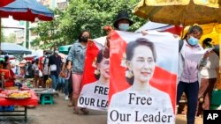 FILE: Protesters walk through a market with posters of ousted Myanmar leader Aung San Suu Kyi in Yangon, Myanmar Thursday, April 8, 2021. She went on trial Monday, May 2, 2022, in a new corruption case against her, alleging she took $550,000 in bribes from a construction magnate.